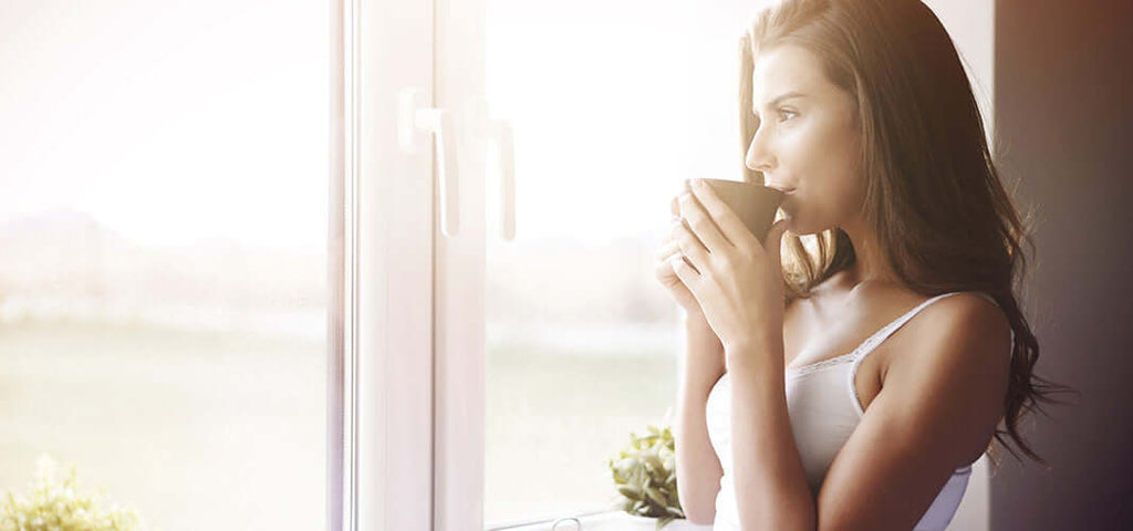 Woman drinking coffee thoughtfully by a sunny window representing thinking about sex and improving love life