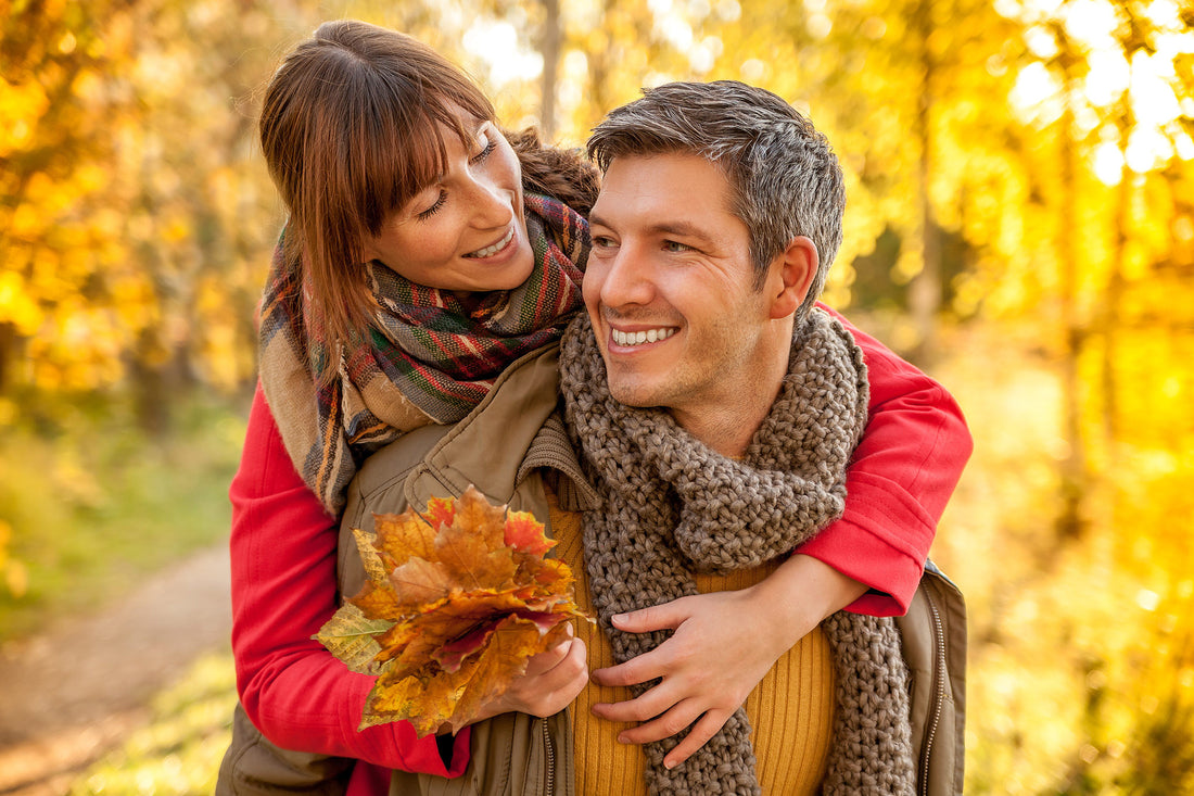 Happy couple embracing outdoors in fall with vibrant autumn leaves, cozy scarves, and warm sunlight, evoking the Pumpkin Spice Latte season atmosphere.
