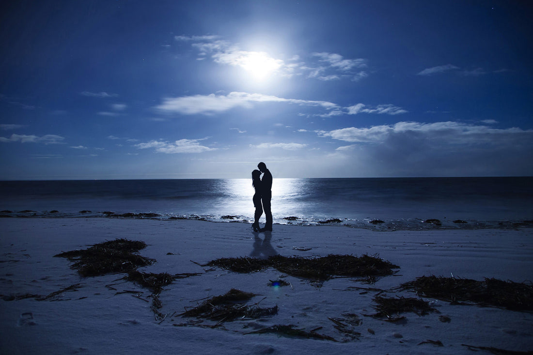Romantic couple embracing on a beach at night under the moonlight, symbolizing a summer sex bucket list scenario.