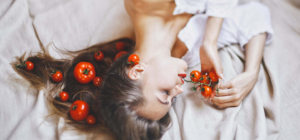 Woman lying on bed with tomatoes in her hair and holding cherry tomatoes, symbolizing aphrodisiac foods to boost sex drive