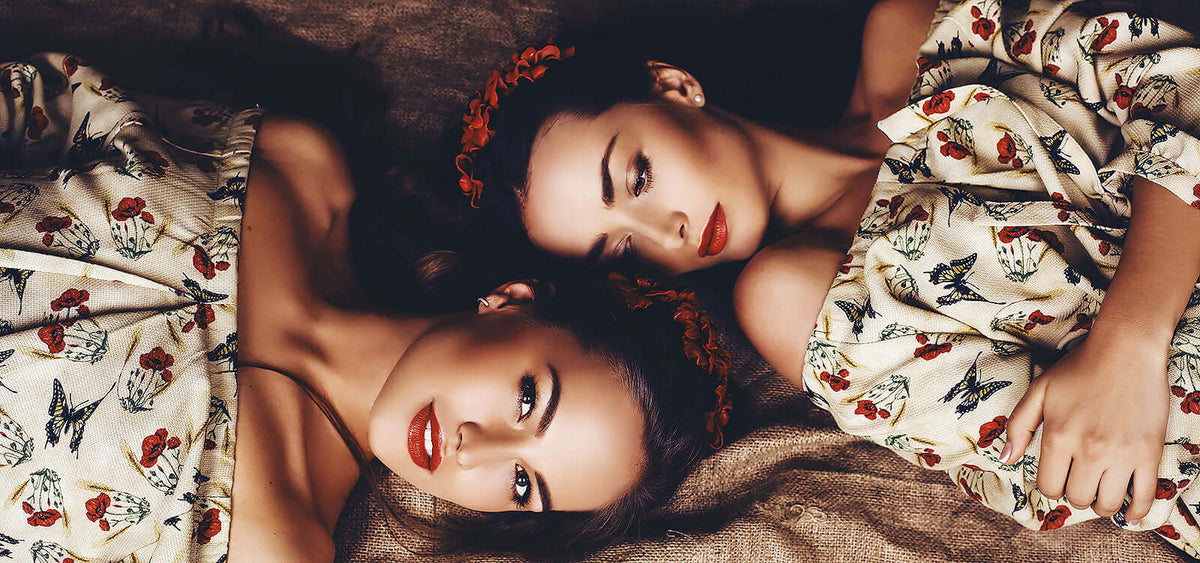 Two women with red lipstick lying on a bed wearing floral patterned dresses representing intimacy and connection