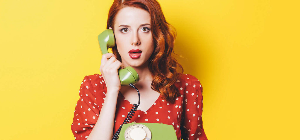 woman with red hair in polka dot dress holding green retro phone handset against yellow background