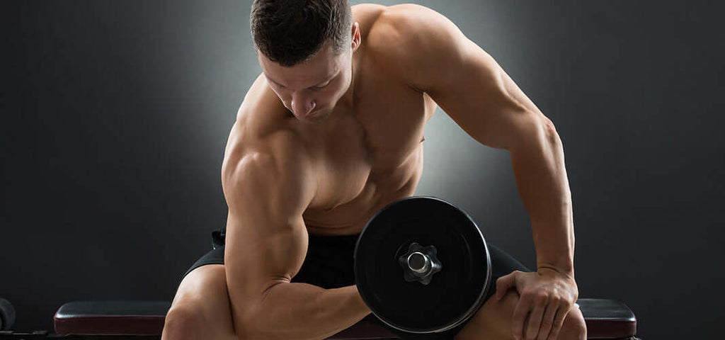 Muscular man performing dumbbell exercise in gym highlighting strength and fitness benefits of Kegels for women.