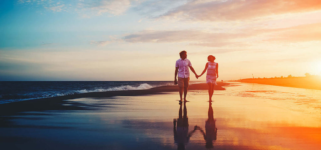 couple walking hand in hand on a beach at sunset reflecting on wet sand