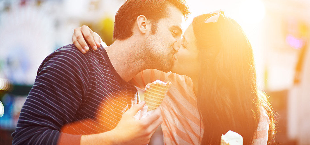 Couple enjoying ice cream and sharing a kiss outdoors in warm sunlight