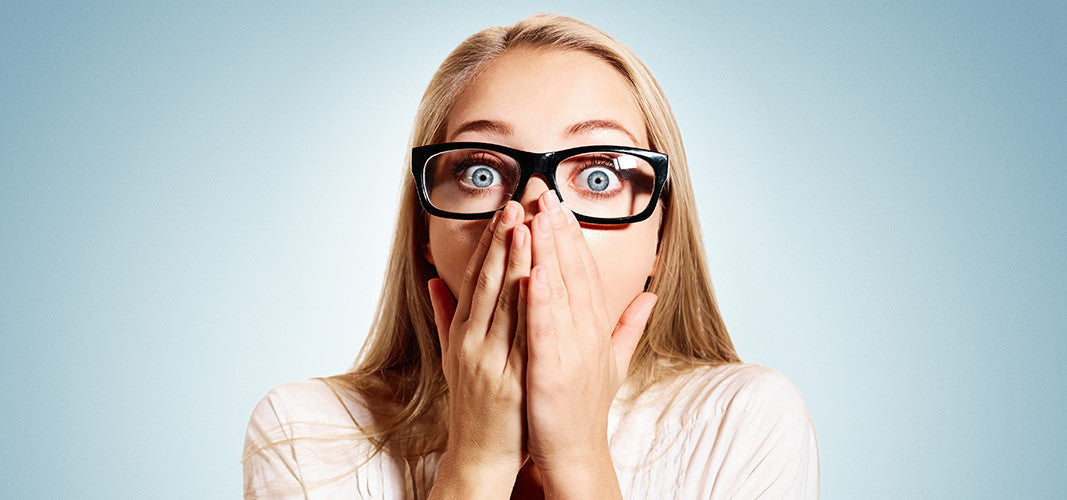 Surprised woman wearing glasses covering mouth with hands against blue background representing masturbation misconceptions concept