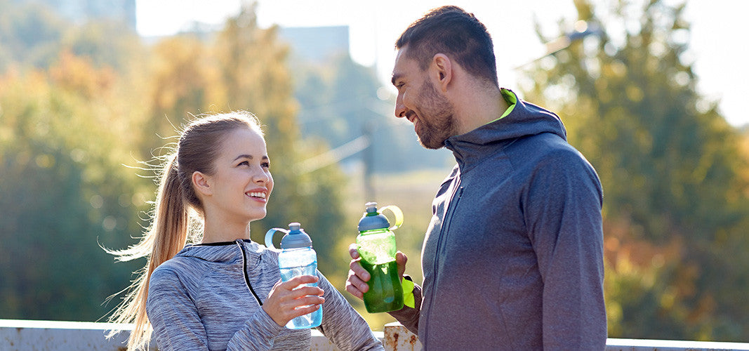 Couple in workout clothes smiling and holding water bottles outdoors after exercising for better sex