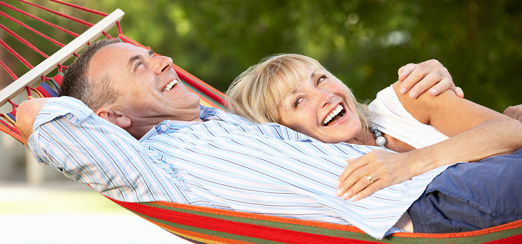 Middle-aged couple laughing and relaxing together in a colorful hammock outdoors on a sunny day