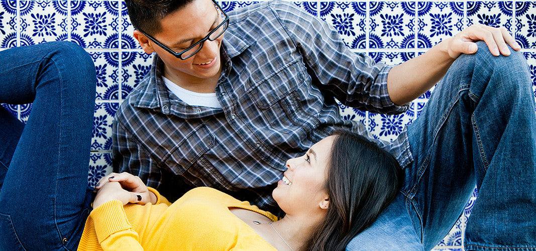 Happy couple lying on patterned tile floor holding hands and looking at each other, representing connection and 5 sex languages concept