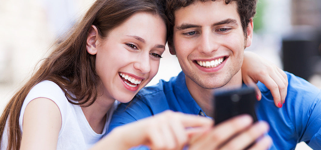 happy young couple smiling and looking at smartphone screen together playing Pokemon Go outdoors