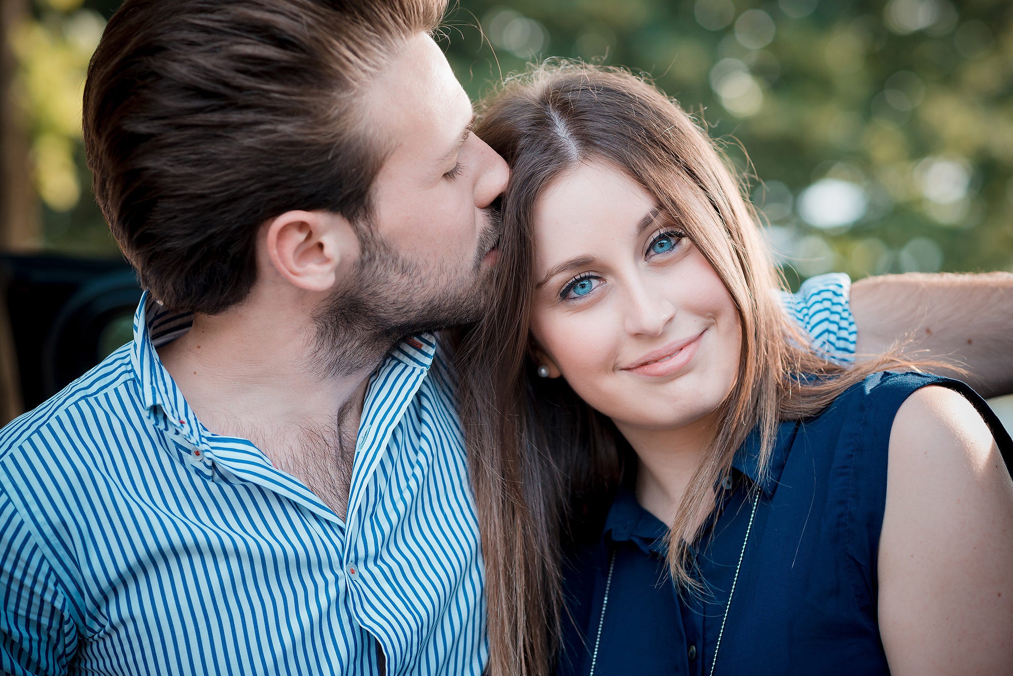 Happy young couple enjoying intimate moment outdoors with man kissing woman on the cheek in natural setting