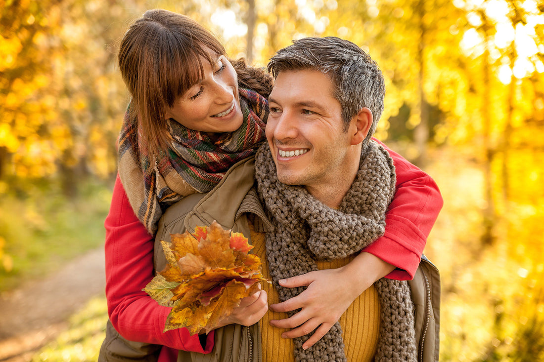 Happy couple enjoying autumn walk embracing each other with fall foliage in background